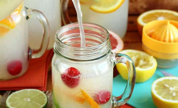 pitcher of lemonade pouring into a glass with citrus fruit