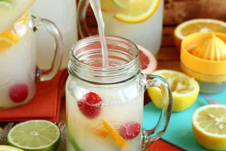 pitcher of lemonade pouring into a glass with citrus fruit